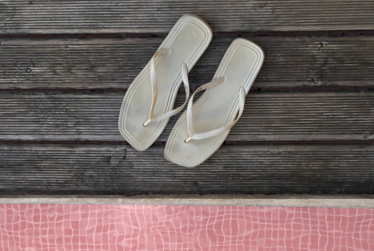 Une paire de tongs posée sur une terrasse en bois au bord d'une piscine : porter des tongs à la piscine et dans les douches collectives limite le risque d'attraper une verrue plantaire, un virus contagieux qui se transmet sur les sols humides.