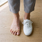 Écarteur d'orteils sur un pied nu, à côté d'un pied en basket